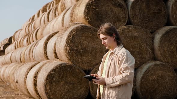 Farmer Agronomist Checks Hay Bales on the Wheat Field After Harvest at Sunset