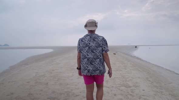Back View of an Adult Man Tourist Walking By the Sea on a Sandy Spit of Island Coast on Gloomy Day