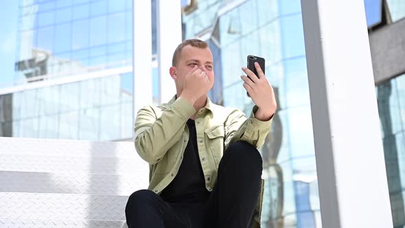 Young Man Sitting on the Stairs and Talking Sign Language Via Video Link on Smartphone Outdoors