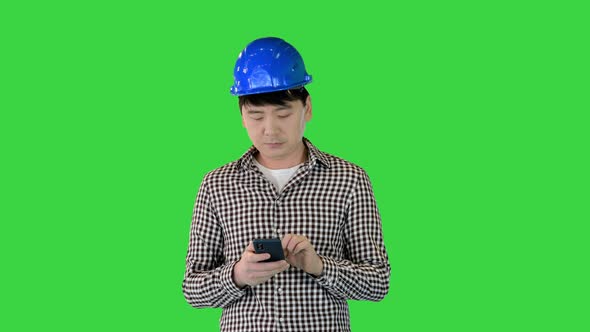 Smart Asian Engineer Holding Smartphone and Using It on a Green Screen Chroma Key