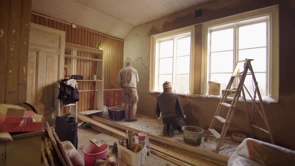 TRACKING shot R2L of 2 men plastering walls with clay, home improvement