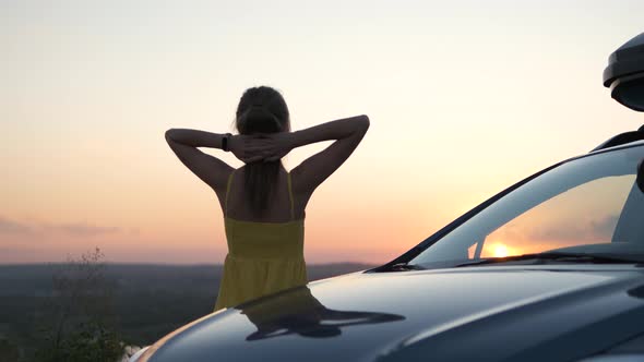 Young female driver in summer dress standing near her car enjoying nature sunset view. Travel 