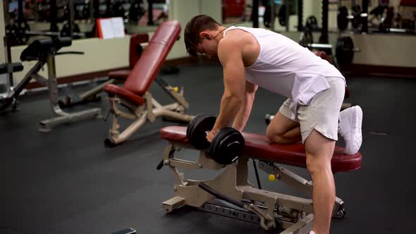 Rear side shot of young bodybuilder doing one arm dumbbell rows using a bench.