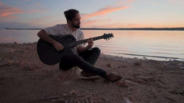 Spanish Caucasian Man Playing the Guitar on the Beach By the Lake at Sunset