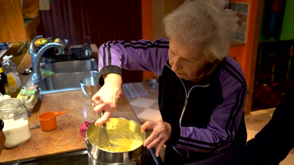 Elderly woman stirring sabayon mixture for tiramisu in a home kitchen.