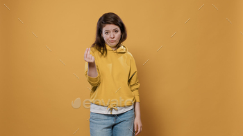ng for money to do shopping doing pay greedy hand gesture in studio. Cunning young adult demanding cash over yellow background.