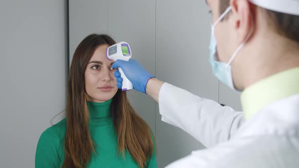 Male Doctor in Protective Face Mask and in Glovesscanning Forehead of Female Patient with Digital