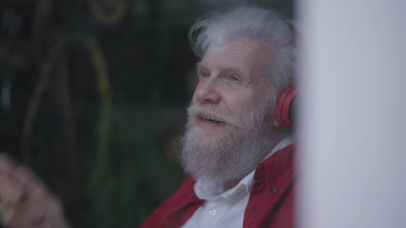 Headshot of Joyful Happy Smiling Old Bearded Man Listening to Music in Headphones Smiling Imitating