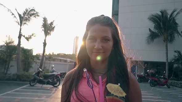 Girl Holds Drink in Hand Smiling By Hotel at Back Sunshine