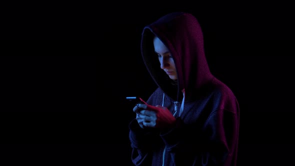 A Young Woman in a Hood with a Phone in Her Hands. Hacker Makes a Hack Through the Phone