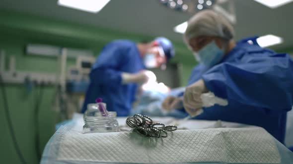 Operating Scissors on Table with Surgical Instruments in Surgery Room with Blurred Nurse and Doctor