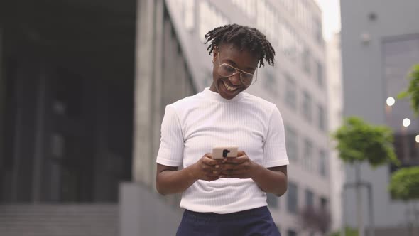 African American Woman Standing Near Modern Business Center with Smartphone in Hands