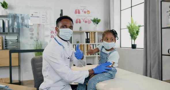 Doctor and Cute Small Black-Skinned Girl Both in Protective Masks Posing on Camera