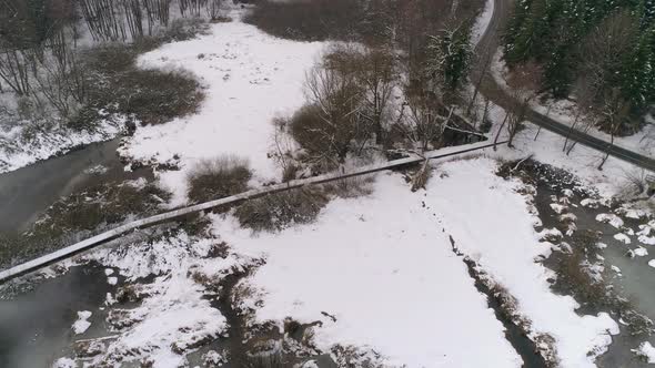 Aerial view of person running over wooden path next to frozen lake with forest covered in snow