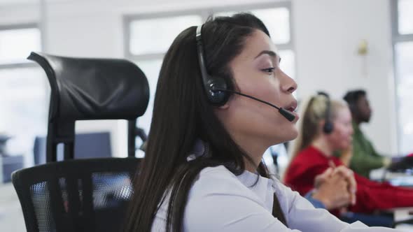 Woman wearing headset talking while sitting on her desk at office