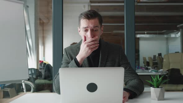 Afraid and Shocked Business Man Looking at Monitor Screen Cover His Mouth with His Hand While