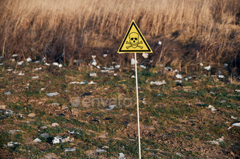 arning about poisonous substances and danger on abandoned territory with trash. Garbage waste field with toxic hazard sign