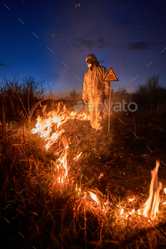 n in suit and gas mask near burning grass with smoke and yellow triangle with skull and crossbones warning sign. Natural disaster concept.