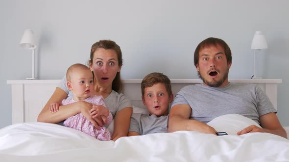 Happy Young European Family with Two Kids Gather on Couch to Watch TV in the Badroom Smiling