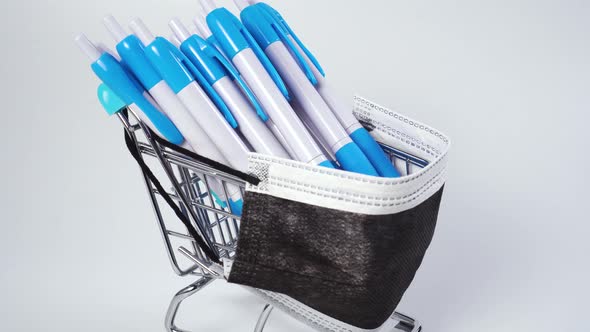 School office pens in shiny shopping cart with black medical protective mask 