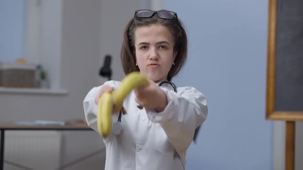 Funny Confident Female Doctor Imitating Gun Shooting with Bananas Laughing Looking at Camera