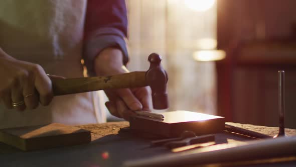 Close up of hands of caucasian female jeweller using hammer, making jewelry