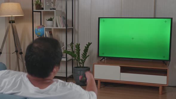 Man Holding Television Remote Control And Watches Green Mock-Up Screen Tv