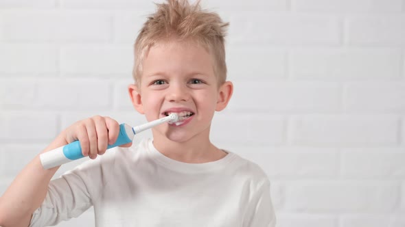 Portrait Happy Smiling Child Kid Boy Brushing Teeth with Electric Toothbrush on White Brick