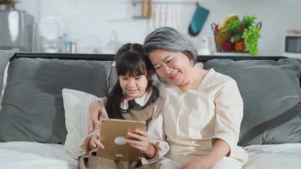 Asian family mother and daughter sitting on sofa enjoy playing game on smartphone together.