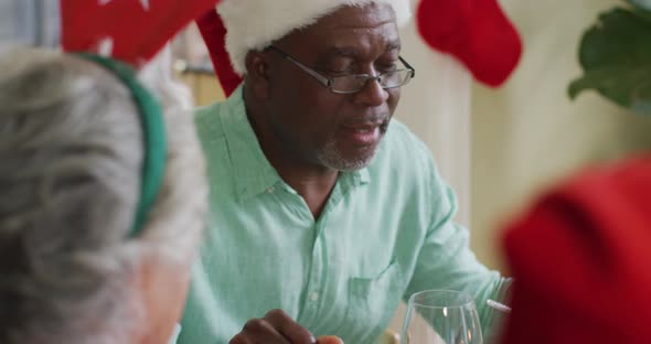 Happy african american senior man praying with friends, celebrating meal at christmas time