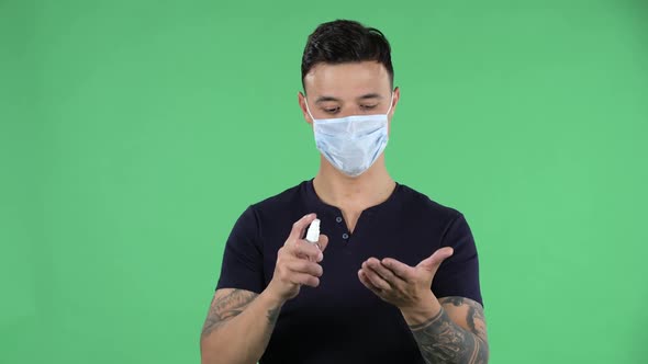 Portrait of a Handsome Young Guy in Medical Protective Face Mask Is Applying Antiseptic on Hir Hands