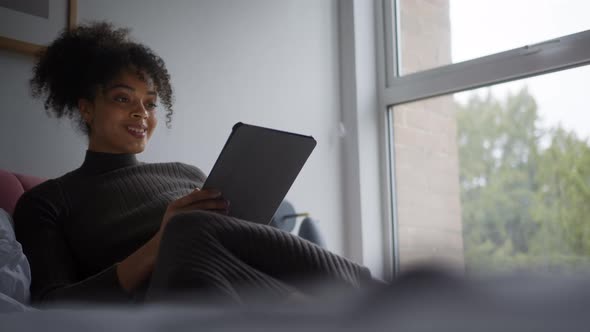 Woman Lying On Bed At Home Making Video Call On Digital Tablet