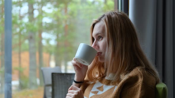 dreamy woman drinking tea by the window overlooking the forest