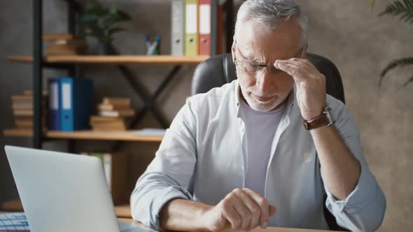 Senior Man is Working at Laptop Taking Off Glasses and Looking Puzzled or Disappointed While Sitting