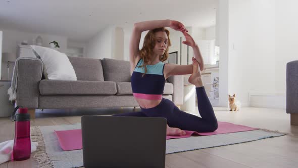 Woman practicing yoga while looking in laptop at home