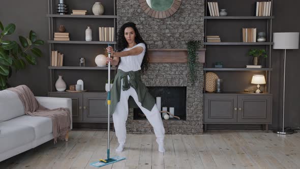 Energetic Hispanic Woman Housewife Cleans Living Room Sings Song Using Mop As Microphone Imagines