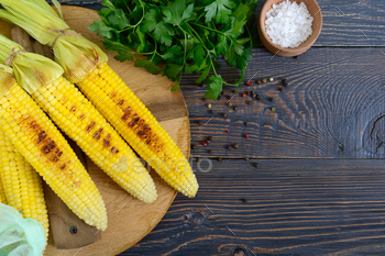 Fresh tasty grilled sweet corn with butter, sea salt and cilantro on a wooden table.