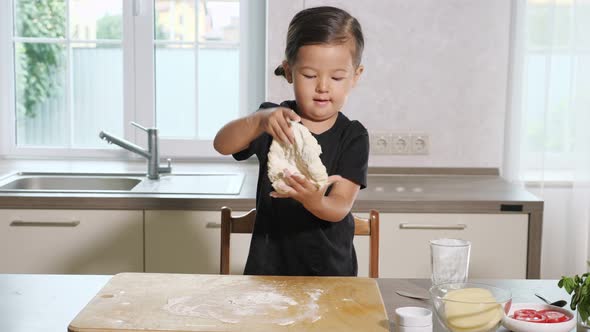 Little Girl Stretching Dough on Wooden Board in Kitchen