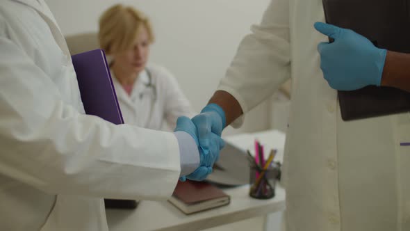 Closeup of Multiracial Male Doctors Hands in Medical Gloves Handshaking in Hospital