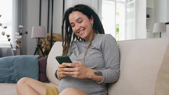 Woman Viewing Funny Photos on Her Phone and Gently Touching Her Pregnant Tummy