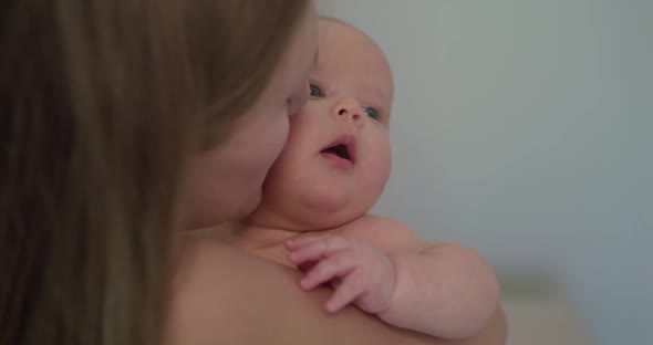 Happy Mother Holds a Little Baby Boy and Kisses Him on Background