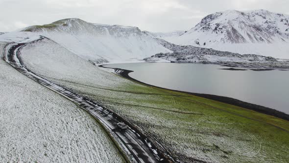 Aerial of a Car Driving on Dirt Road Along Lake and Majestic Mountains Iceland