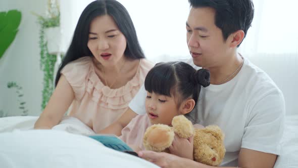 Happy Asian family, Parents spend leisure time with young little kid daughter in bedroom at house.