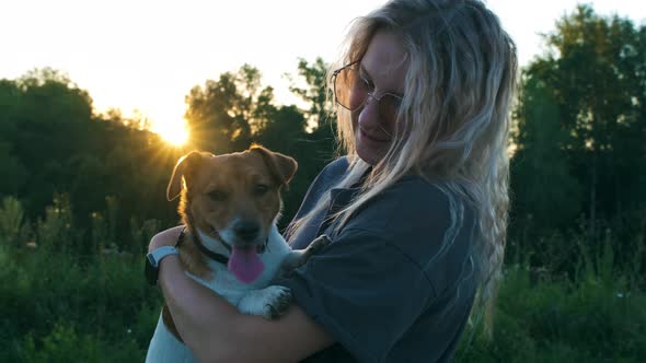 Young woman holding on her hands Jack Russell Terrier. Sunset. Slow motion