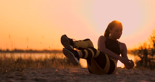 Young Beautiful Woman Athlete Practicing on the Beach Doing Exercises for the Muscles of the Abs at