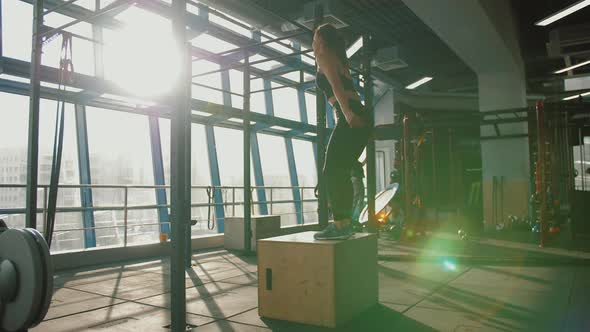 Young Woman Jumping Into Wooden Box in Crossfit Training at Gym