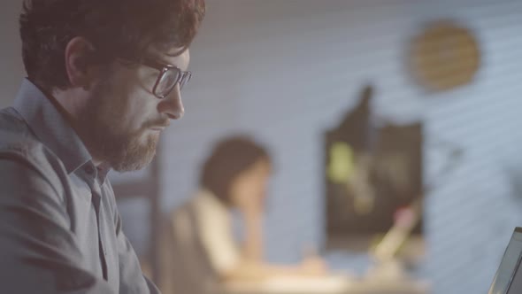 Man in Glasses Working on Laptop in Dark Office