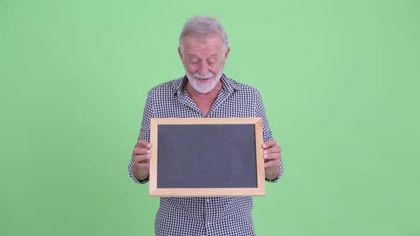 Happy Senior Bearded Man Holding Blackboard and Looking Surprised