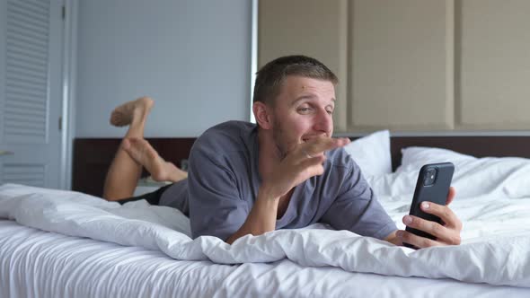 A Caucasian Man Laying Down on a Bed Video Chatting with Beloved Ones