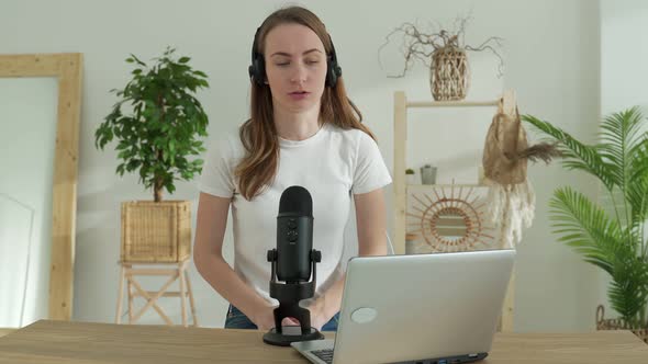 Woman Speaking Into a Microphone in a Recording Studio Smiles While Creating a Podcast for an